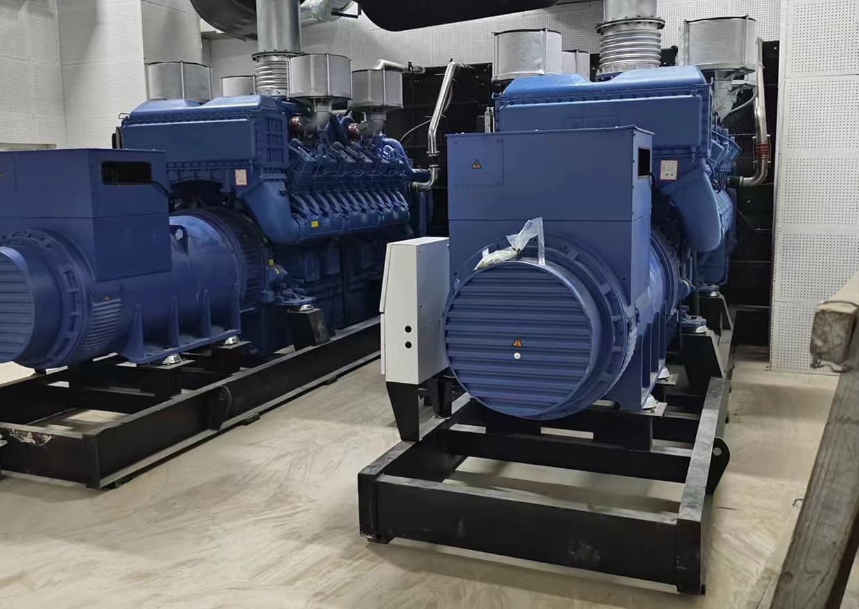 Two blue open-type sets on parallel skids with a synchronising cabinet between them in a plant room