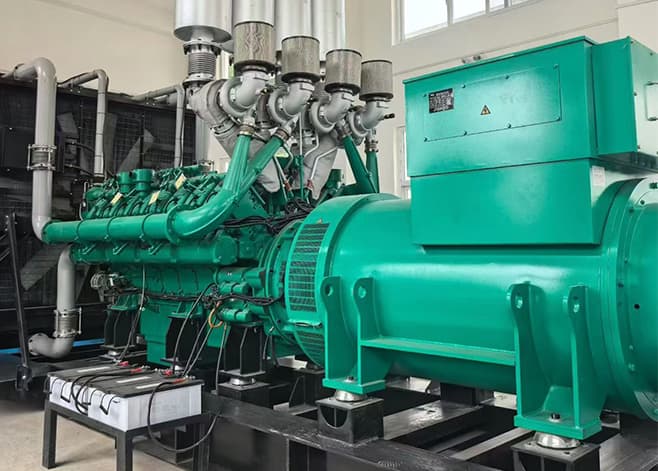 A green high-voltage genset with a large alternator and exhaust manifold inside a plant room