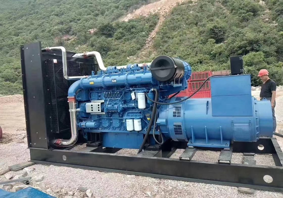An open-type 800 kW set on a black steel skid standing on a gravel bench with forested hills behind