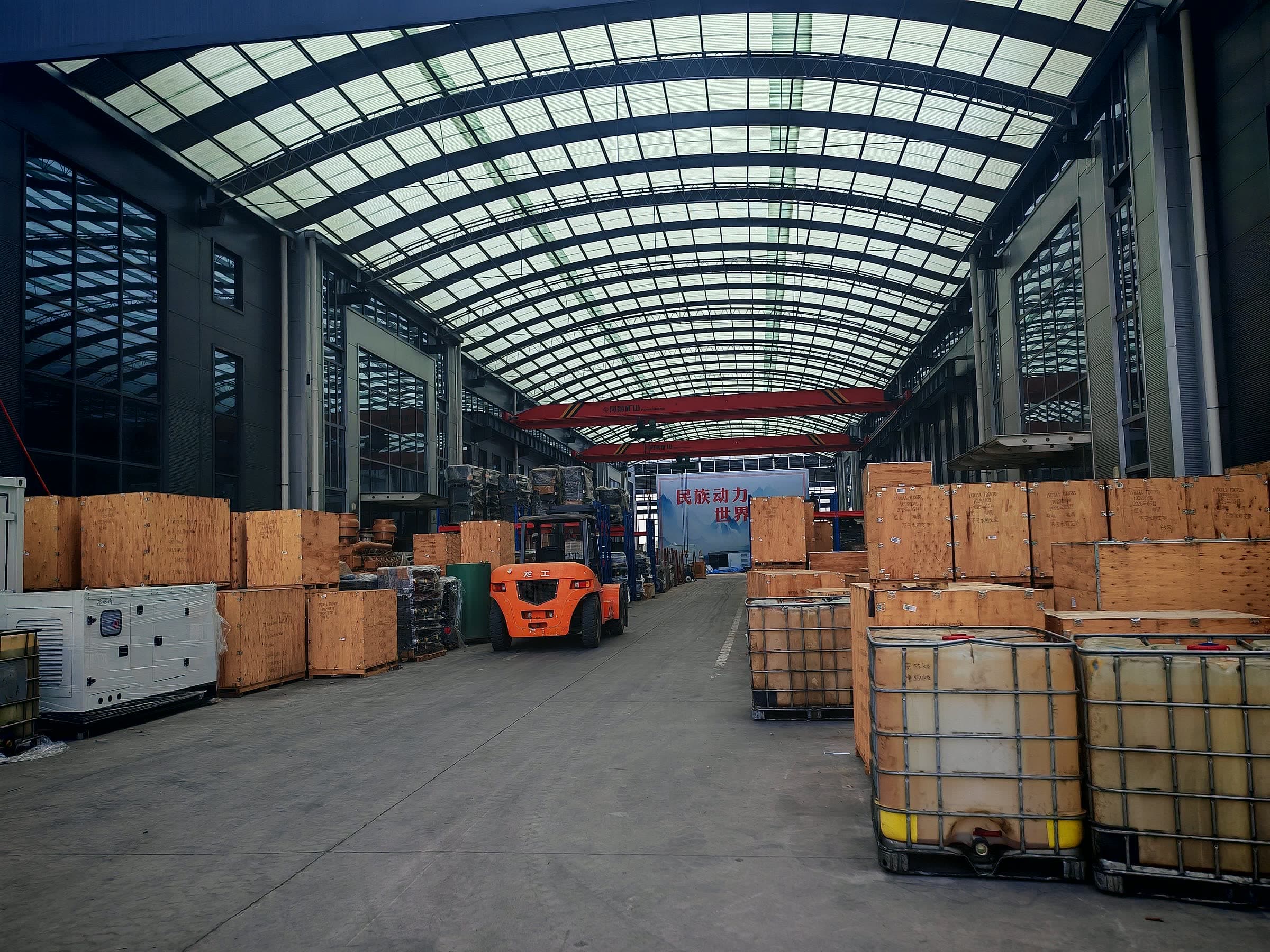 Wide workshop hall with export crates stacked both sides, IBC totes on the right and a forklift in the aisle
