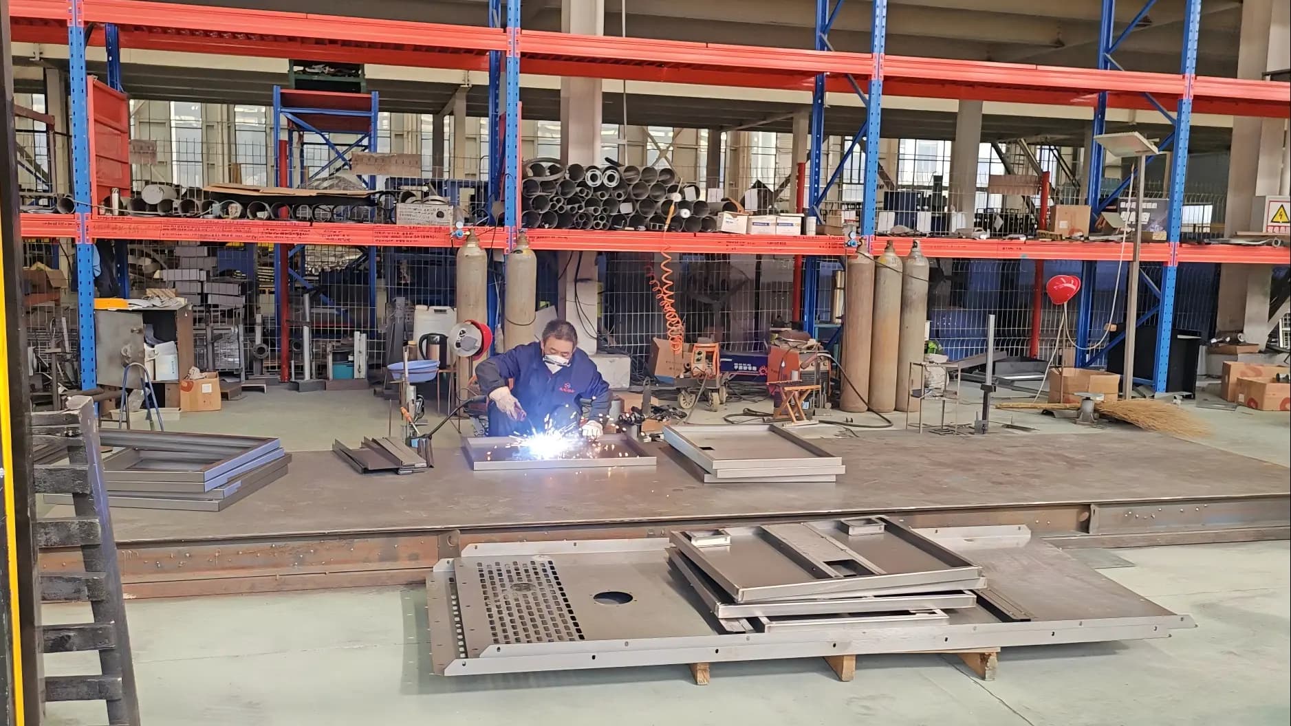A welder working on a steel canopy panel in the welding workshop